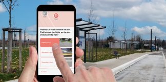 Ein Smartphone wird vor einer Bushaltestelle hochgehalten, im Display stehen Fragen.