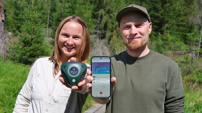 Eine FRau und ein Mann stehen nebeneinander im Wald. Sie hält ein elektronisches Gerät in der Hand, er ein Smartphone.
